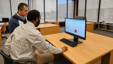 Two users on a computer, one showing the other user what to do.