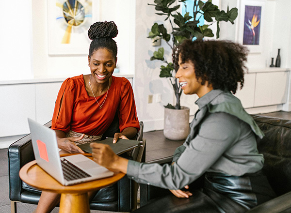 Two professionally-dressed adult women looking at a laptop and laughing