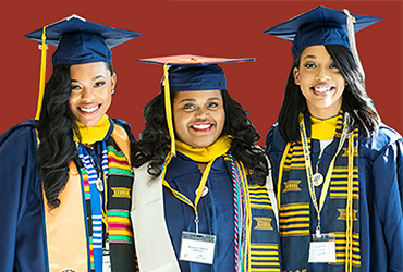 three females in UDC commencement regalia