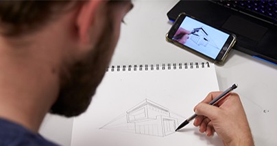 A man concentrates on drawing a house in a sketch notebook