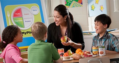 A teacher shows children how to eat healthy foods in a fun and engaging classroom setting.