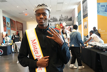 Young man wearing a crown and holding up his hand.