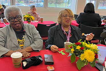 Two UDC staff people sitting at a table, eating breakfast and smiling.