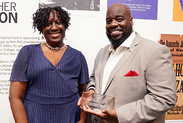 Two people smiling. One is holding an award.