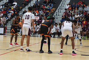 UDC men's basketball team playing a game in a gym.