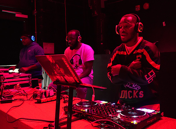 Three djs in a darkly lit room.