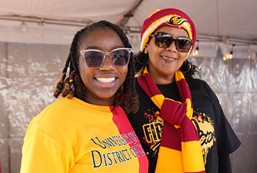 Two women standing outside wearing red and gold outerwear.